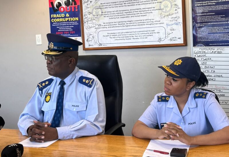 Two police officers sit at a wooden table beneath an anti-corruption pledge and code of conduct posters, conveying professionalism and integrity.