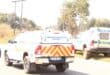 Forensic pathology service pickup with red-yellow chevrons parked beside a police vehicle on a rural roadside, creating a somber scene.