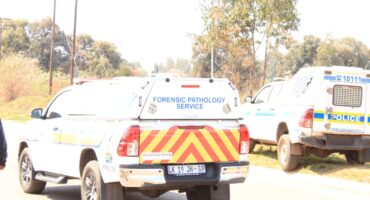 Forensic pathology service pickup with red-yellow chevrons parked beside a police vehicle on a rural roadside, creating a somber scene.