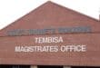 A red-brick gabled facade displays blue “Steve Tshwete Building” and white “Tembisa Magistrates Office” lettering, conveying a formal civic setting.