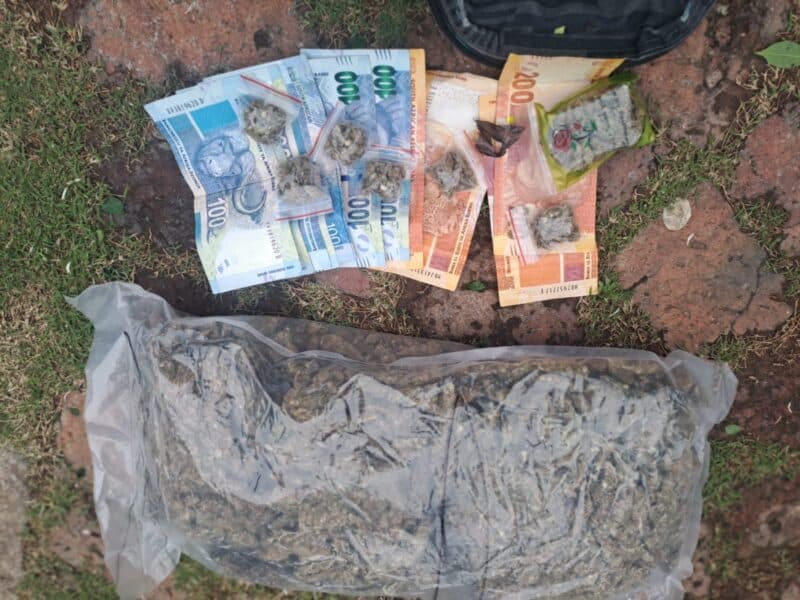 A large plastic bag of dried plant material lies on the ground beside scattered banknotes and small wrapped packets, suggesting a drug seizure.
