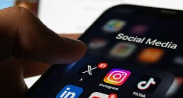 Close-up of a hand holding a smartphone showing social media apps, including Instagram, TikTok, LinkedIn, YouTube, Pinterest, and X.