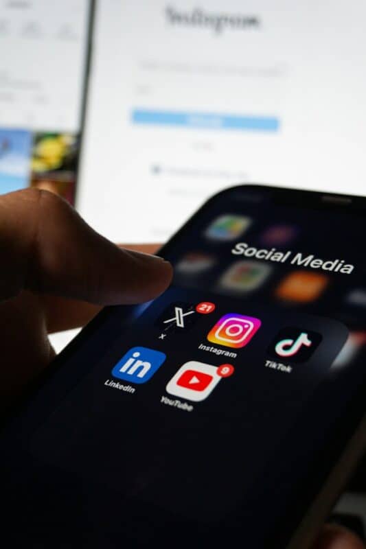 Close-up of a hand holding a smartphone showing social media apps, including Instagram, TikTok, LinkedIn, YouTube, Pinterest, and X.