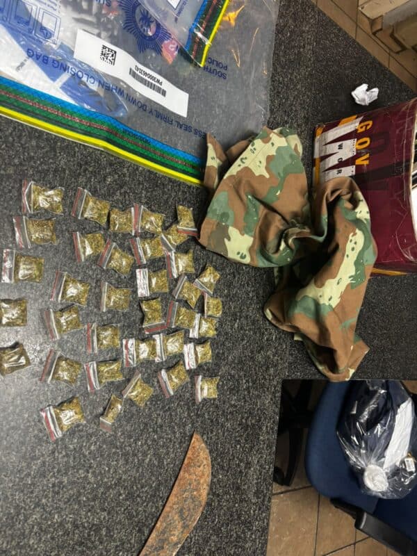 An evidence display shows dozens of small sealed packets, camouflage clothing, labeled bags, and a curved blade on a dark floor, suggesting a police seizure.