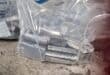Clear labeled plastic bags contain stacked rectangular metal components on a worn concrete floor, creating an industrial, utilitarian scene.