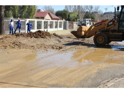 The TLB (earthmover) collects the sand that has been scattered across Botha Street. Another important note, there is no flag person warning motorists of the TLB's presence on the road, this is another requirement of the OHS Act (Operational Health and Safety Act).