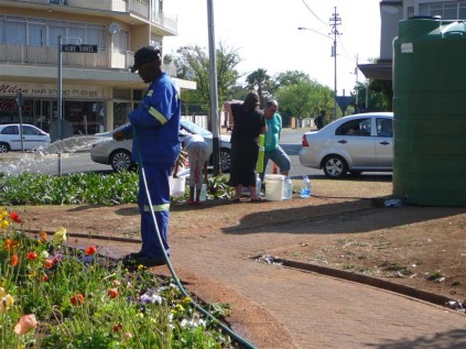 As a metro employee waters the plants at Howe Circle residents wait with buckets and bottles to collect much needed water.
