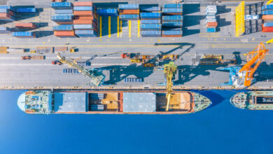 Aerial top view huge cargo ship moored at the pier at the port, loading goods, metal, concrete and other solid raw materials.