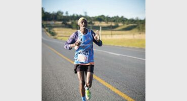 A man running in a marathon with his hands up.
