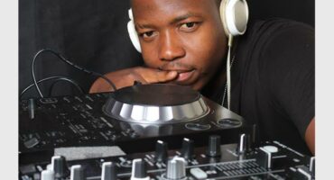 A man wearing headphones and standing next to a dj mixer.