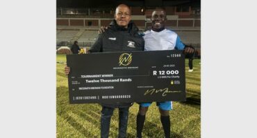 Two men standing on a soccer field holding a large check.