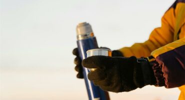 A person wearing gloves holding a blue and yellow bottle.