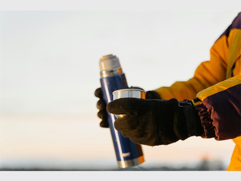A person wearing gloves holding a blue and yellow bottle.