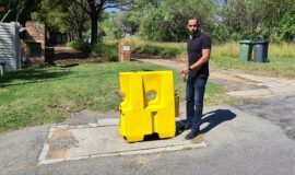 Jay Soudamma points at the manhole covered with a yellow bollard.