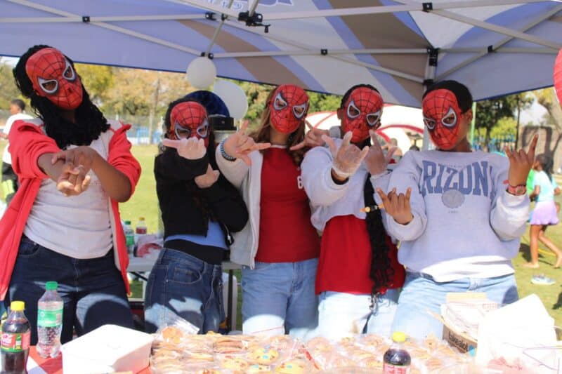 Learners wearing Spider-Man masks pose behind their food stall, adding a playful twist to the day while showcasing the creativity and marketing skills encouraged by the Tickey Day on August 21, 2026.
