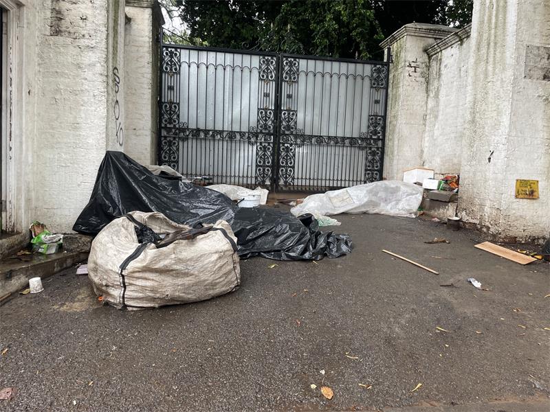 Description: A homeless man lies under tarpaulins and plastic sheeting outside a property on Bombas Road as rain falls, on September 30, 2026.