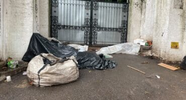 A homeless man lies under tarpaulins and plastic sheeting outside a property on Bombas Road as rain falls on September 30, 2026. Photo: Xoliswa Zakwe