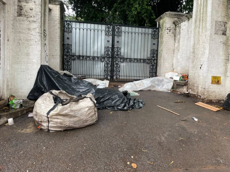 A homeless man lies under tarpaulins and plastic sheeting outside a property on Bombas Road as rain falls on September 30, 2026. Photo: Xoliswa Zakwe