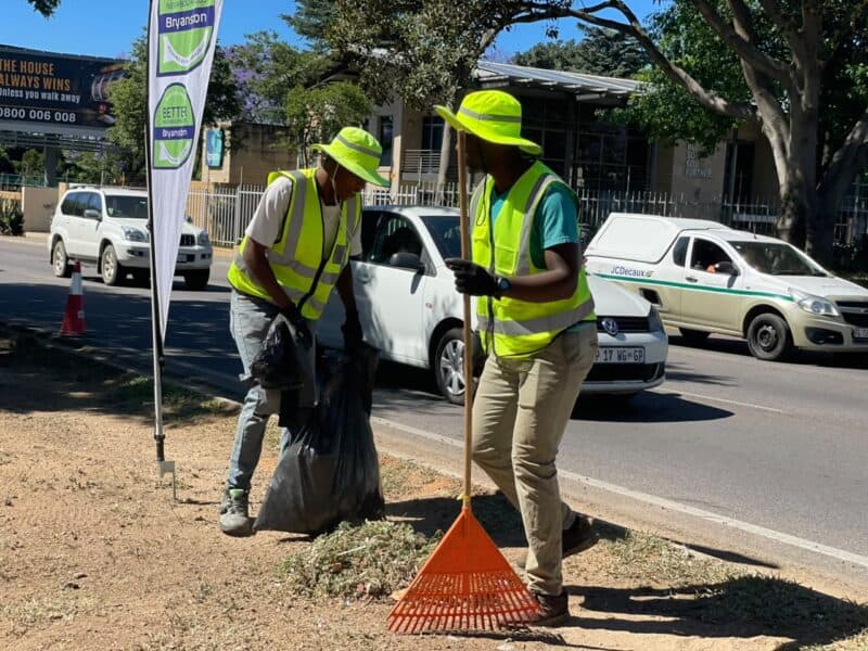 Sive Soul and Mike Ncube clear weeds along Winnie Mandela Drive during the Better Bryanston clean-up on October 23, 2026.