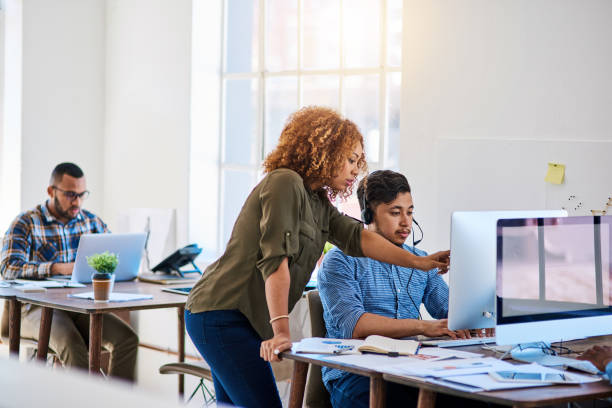 Shot of a young phone operator speaking with a coworker at his desk