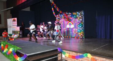 A group of people on stage performing with colorful balloons.