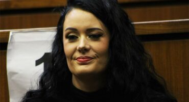 Woman with dark curly hair sitting in a courtroom, smiling confidently.