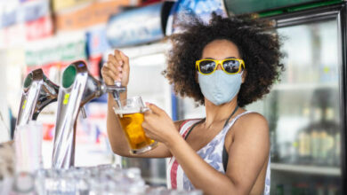Young bartender pouring a draft beer and wearing a protective face mask
