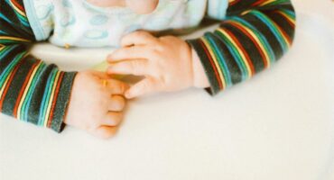 A baby in a high chair with a green and white striped shirt.
