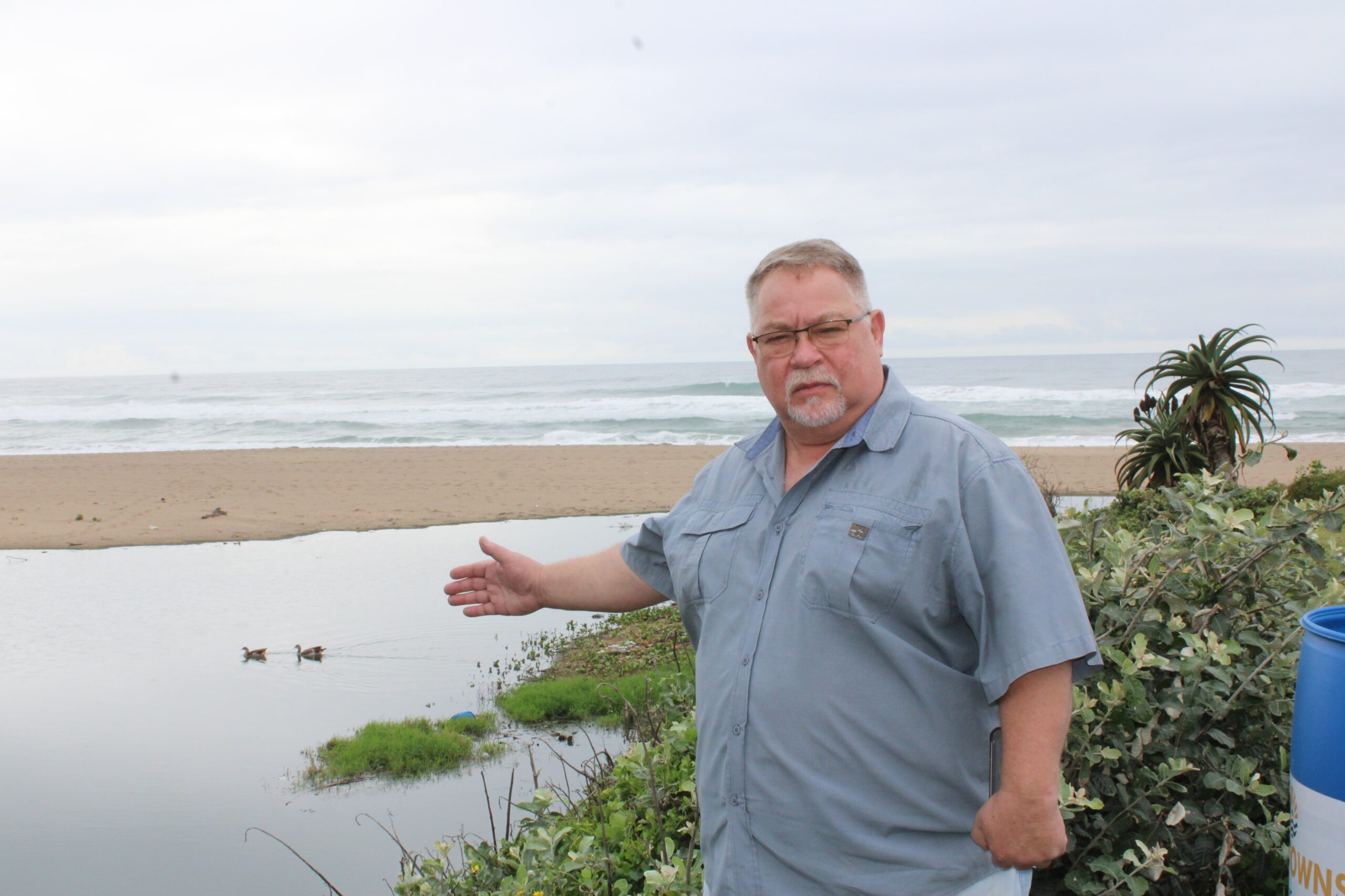 A man pointing toward a river polluted with sewage.