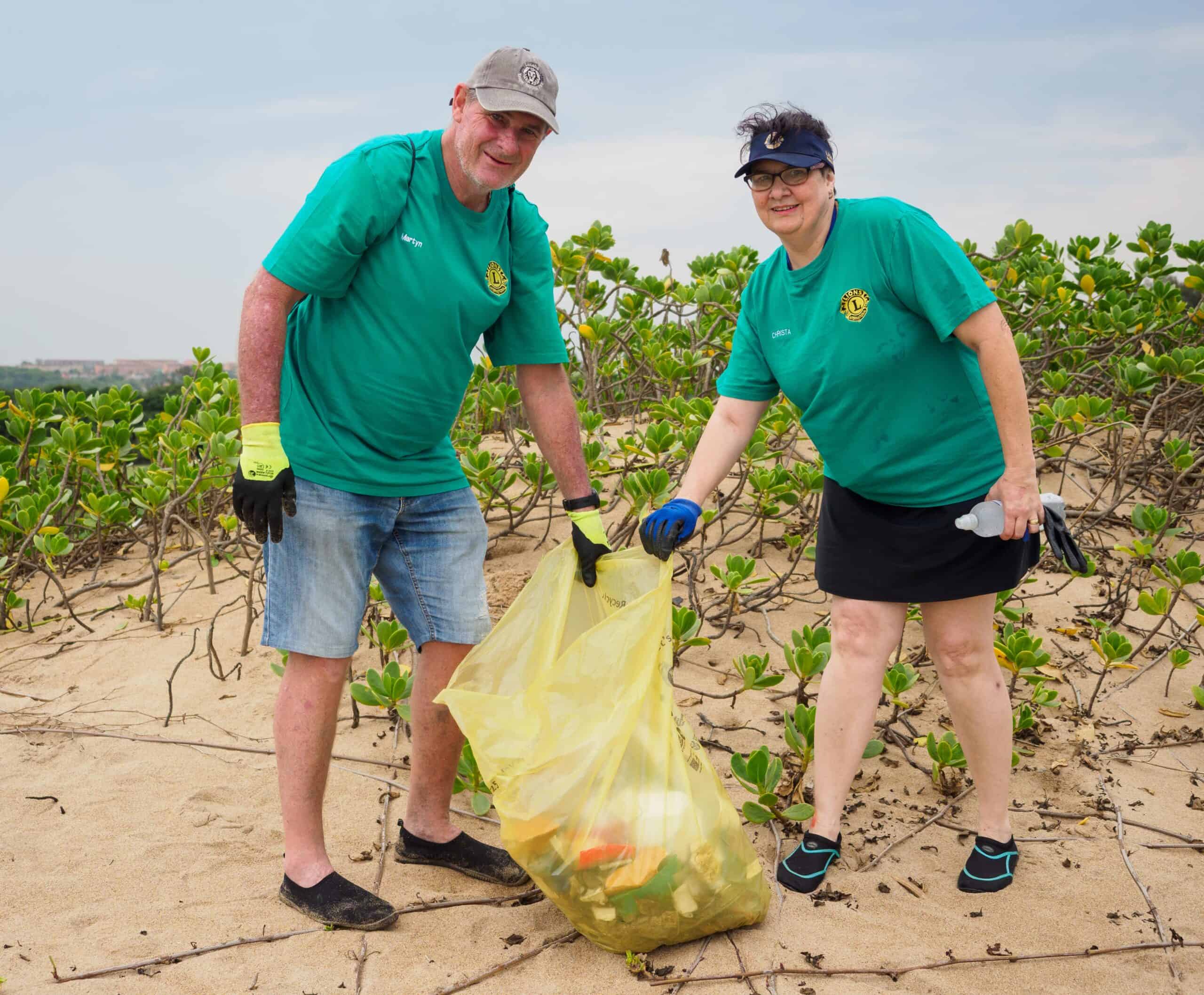Two people cleaning up a beach with a bin bag.