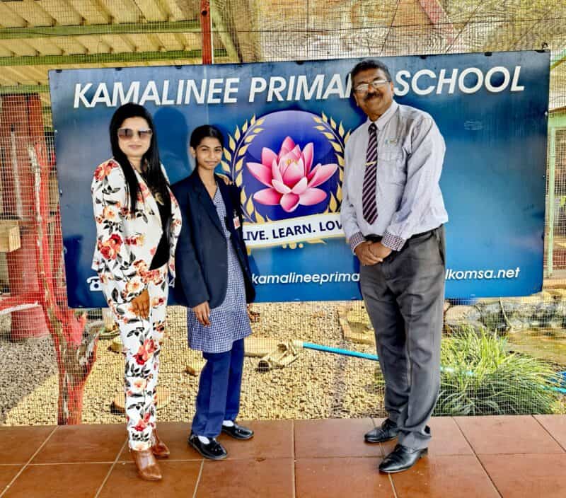A teacher, learner and principal standing in front of the school banner.