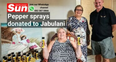 A woman sitting, holding two pepper spray bottles, with two other people standing.A woman sitting, holding two pepper spray bottles, with two other people standing.