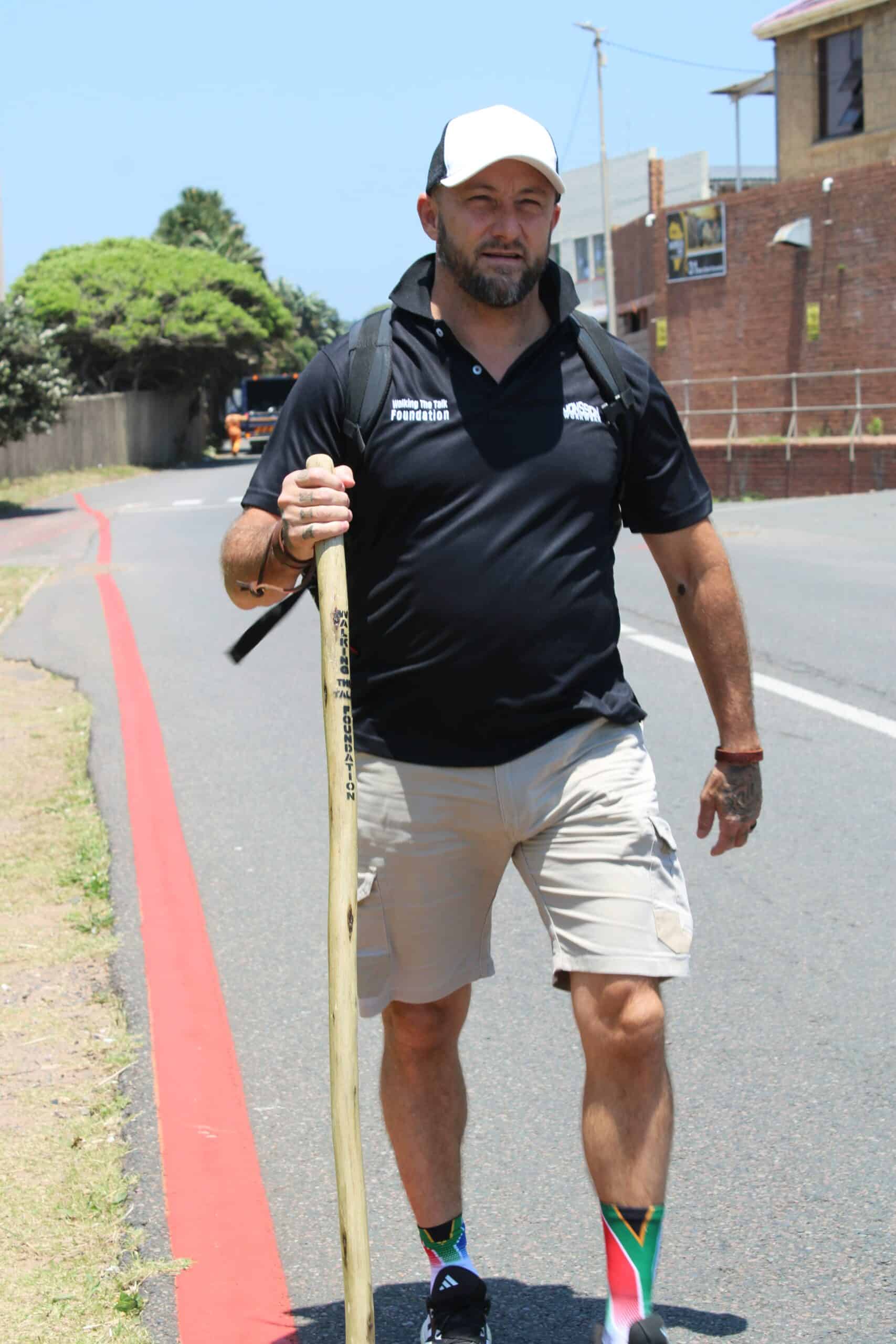 A man walking along the road with a walking stick. 