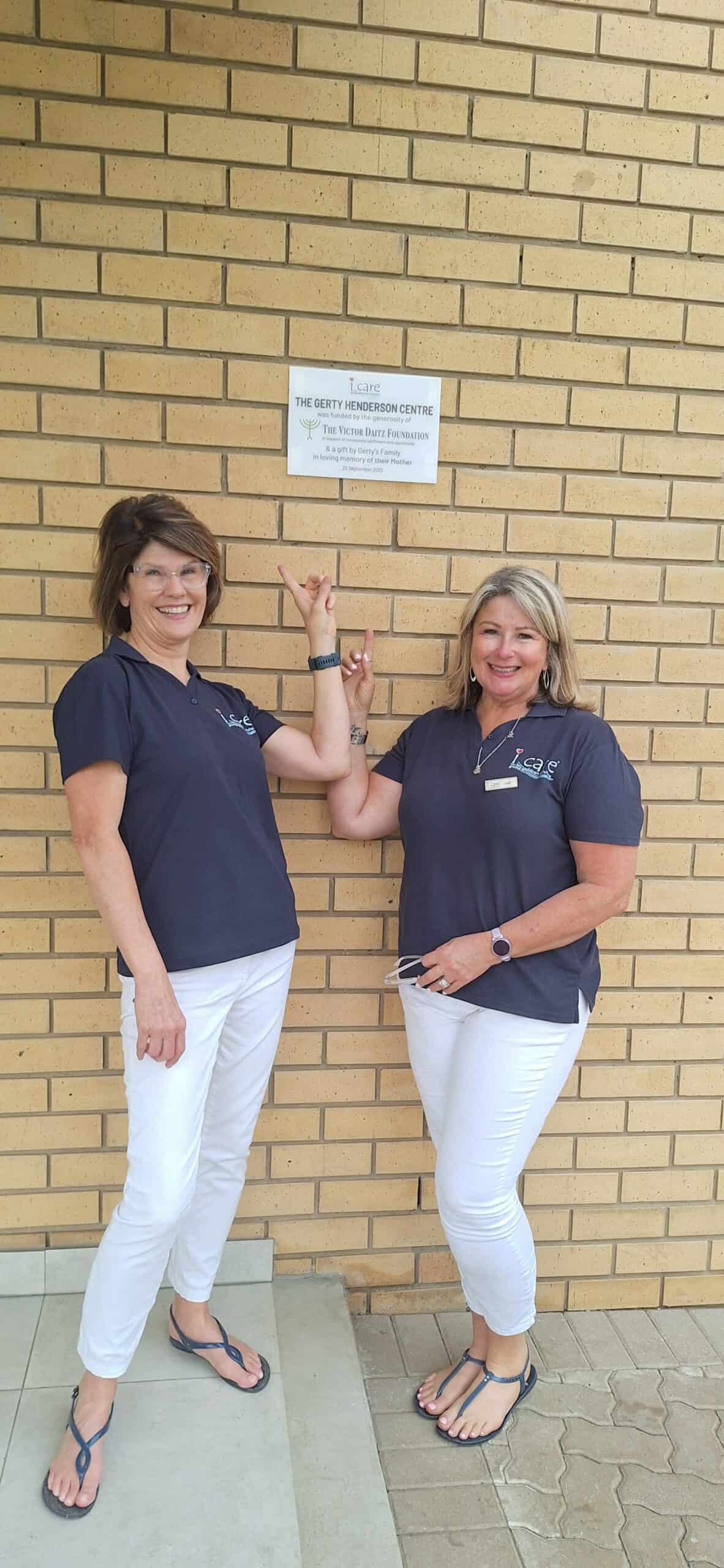 Two women posing under a plaque.