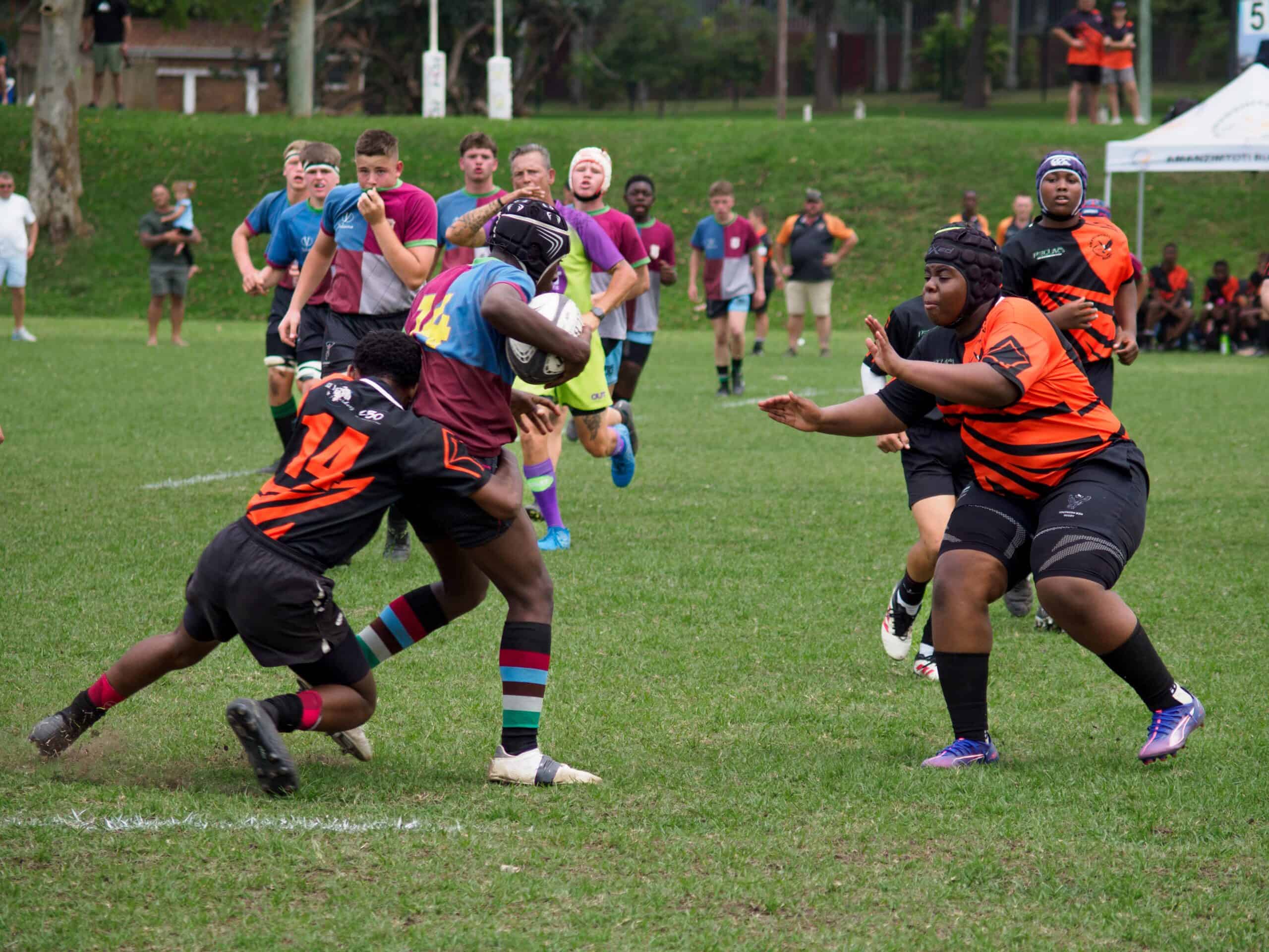 A rugby player tackling another rugby player. A defender is about to tackle as well.