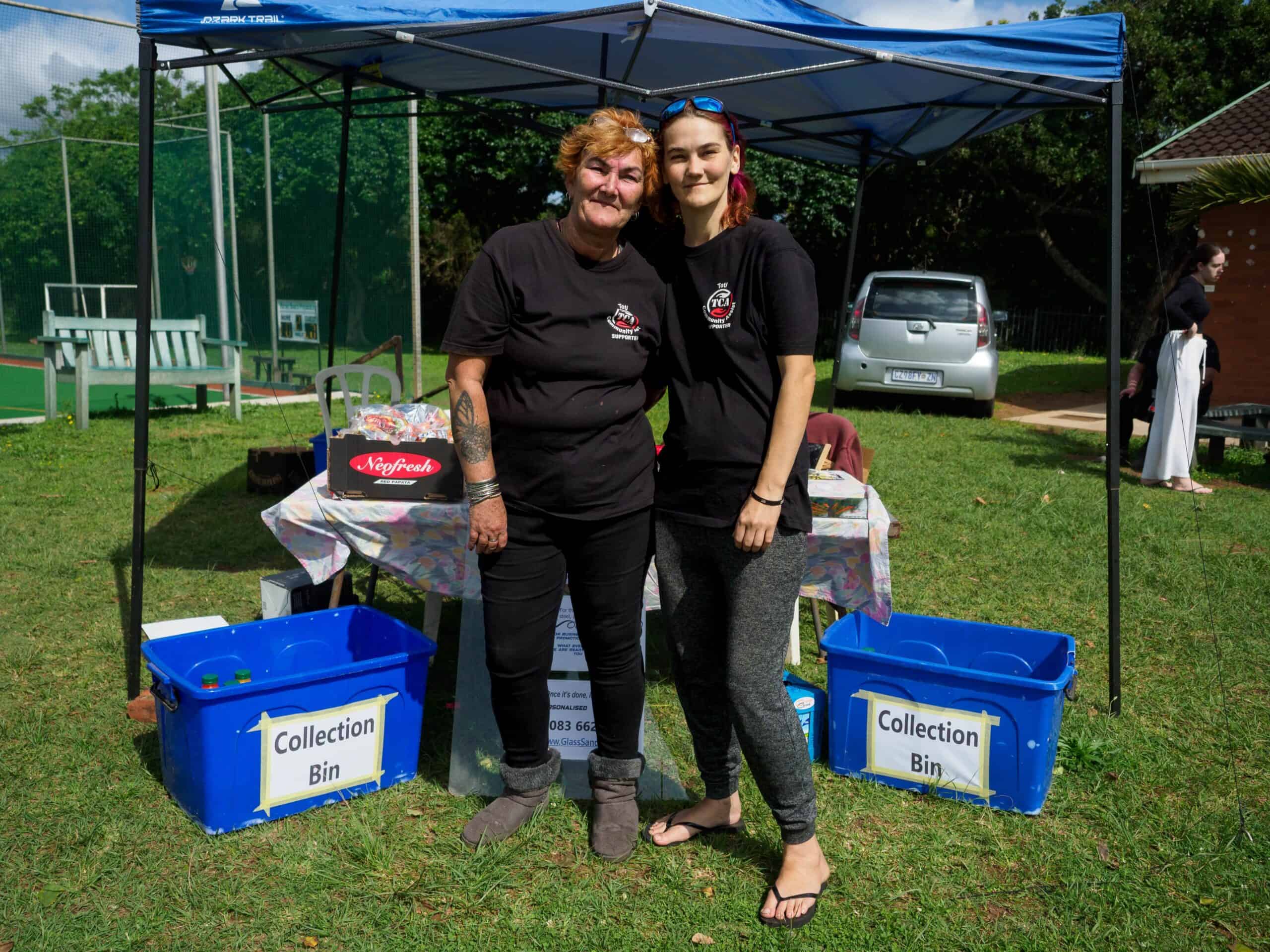 Two women stand in front of a stall at a market day.