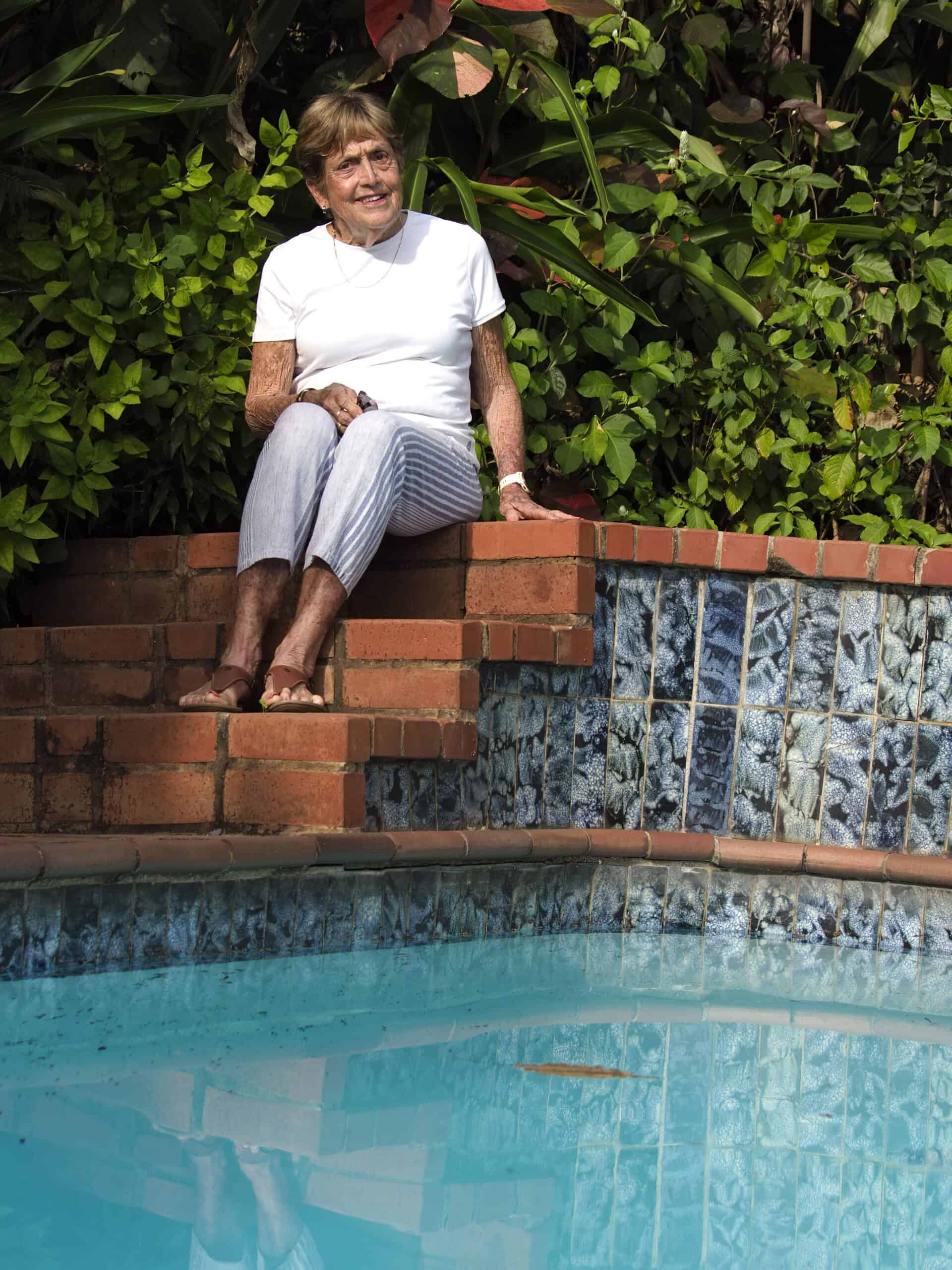 An elderly woman sitting by her pool.