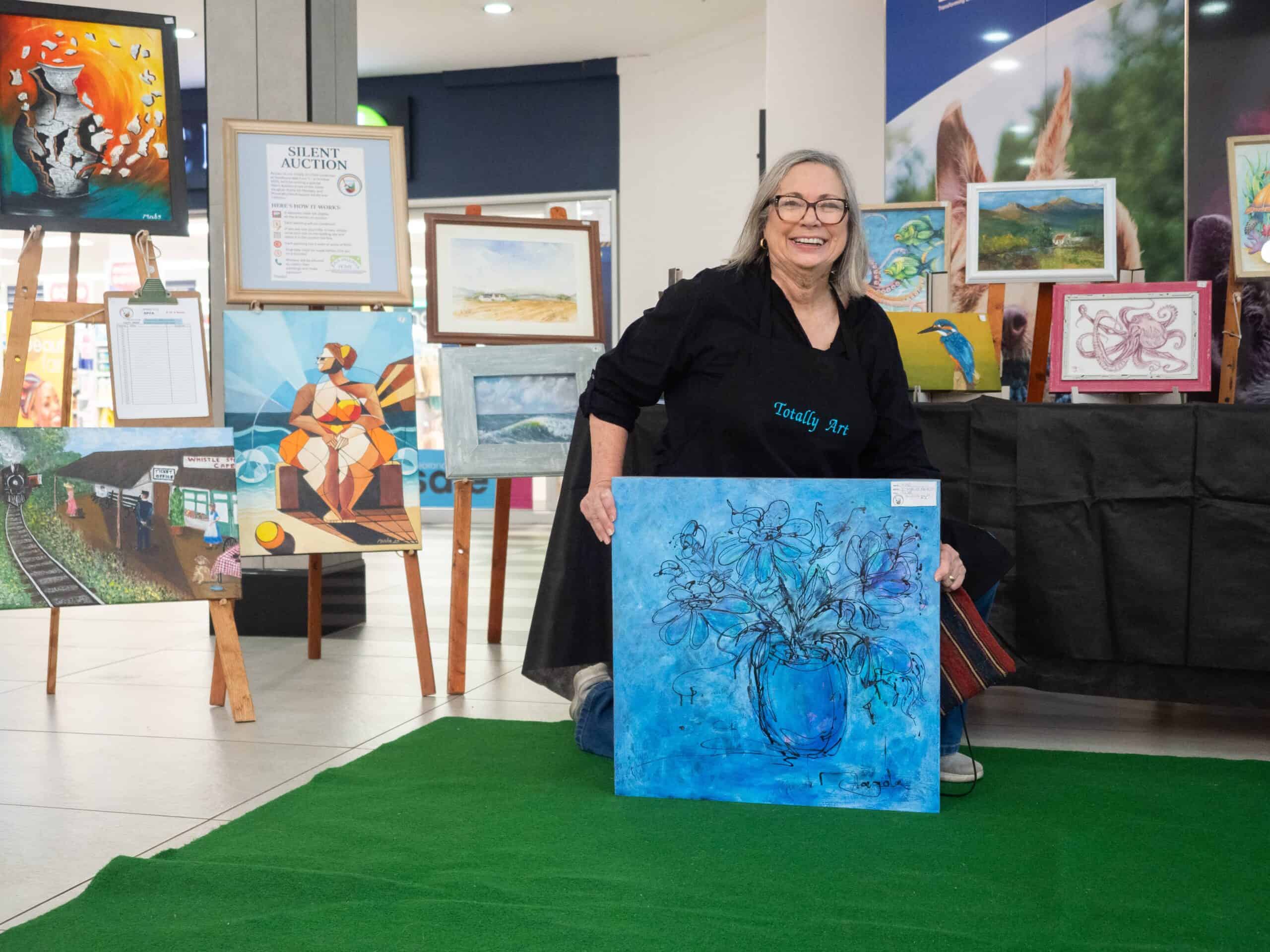 A woman holding up a painting. In the background, there are multiple paintings.