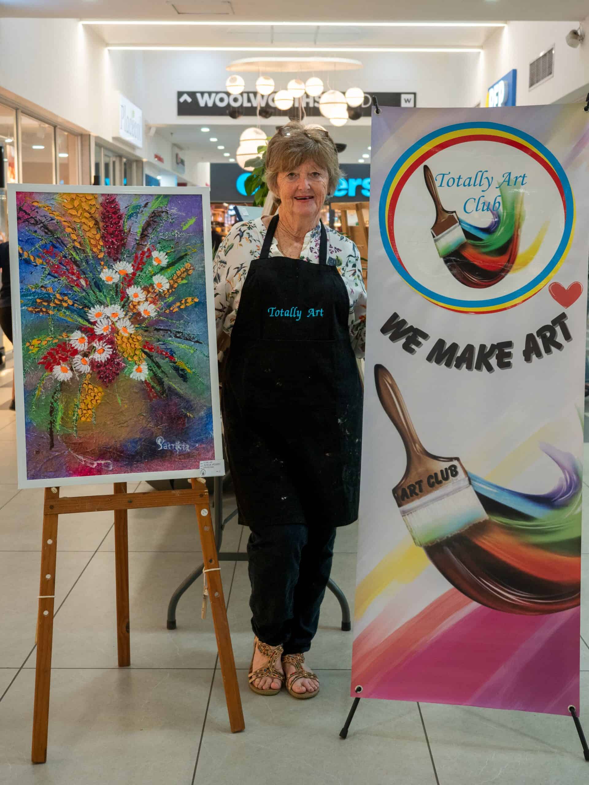A woman next to a banner and her painting.
