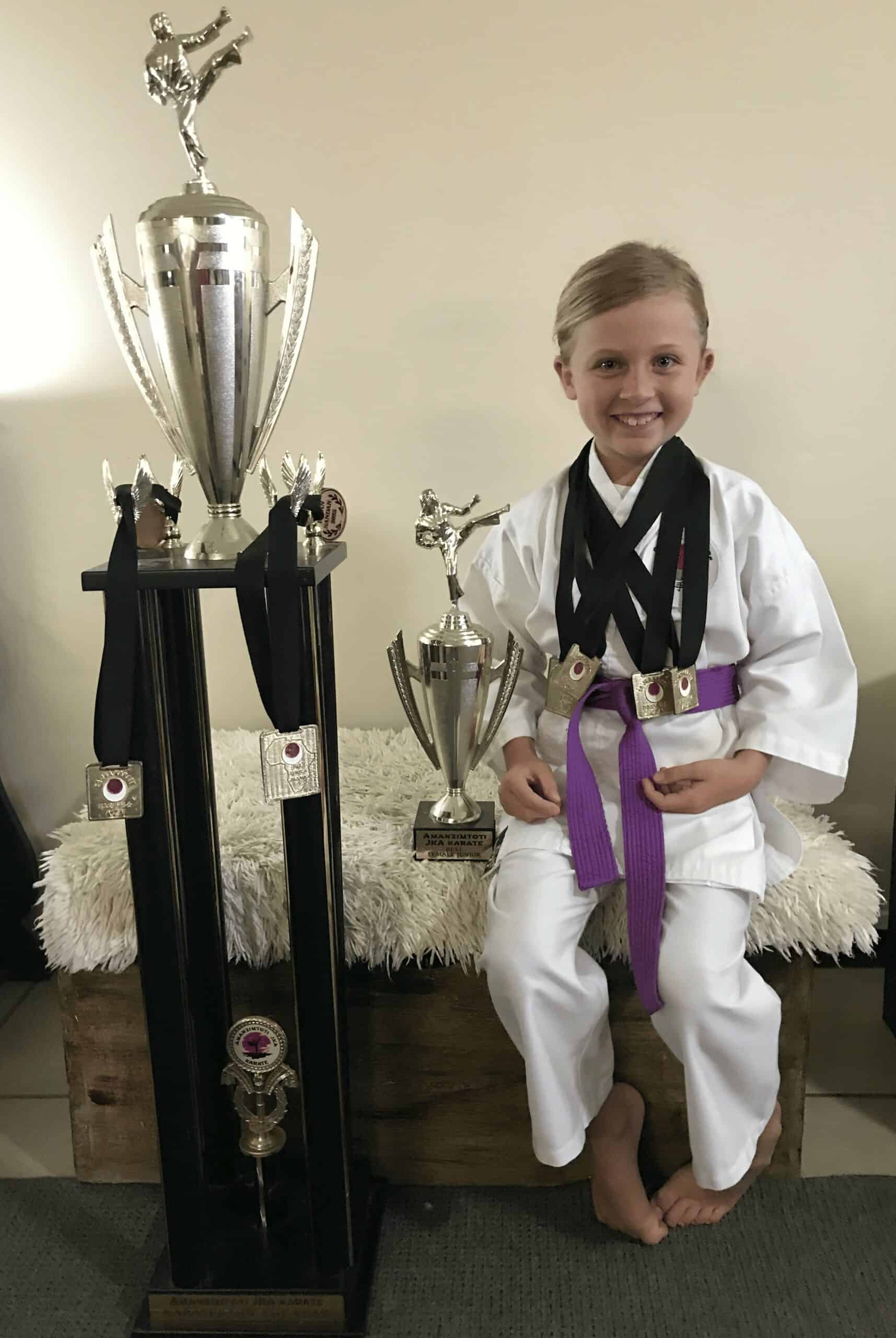 A young girl in karate Ghi, next to her trophies.