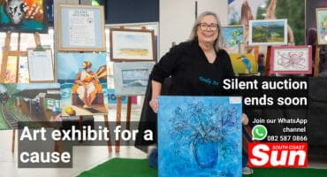 A woman holding up a painting. In the background, there are multiple paintings.