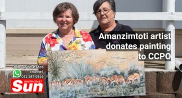 Two woman hold up a painting of Springbok grazing.