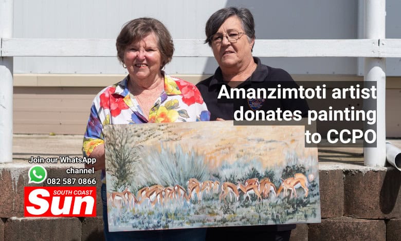 Two woman hold up a painting of Springbok grazing.