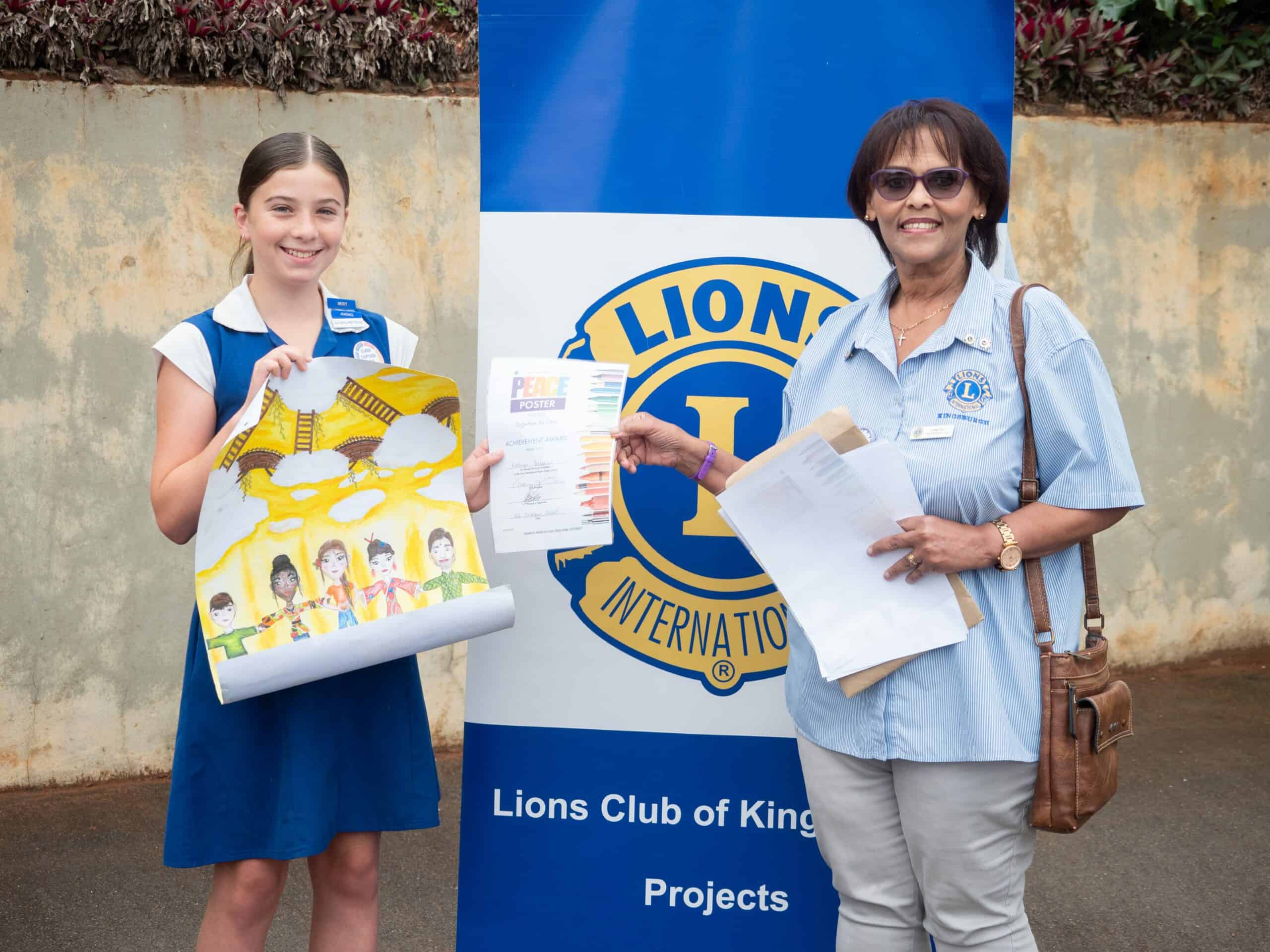 A school child holding up her artwork, receiving her award from another woman.