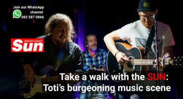 Musicians performing on stage. A bassist, a drummer and a guitarist.