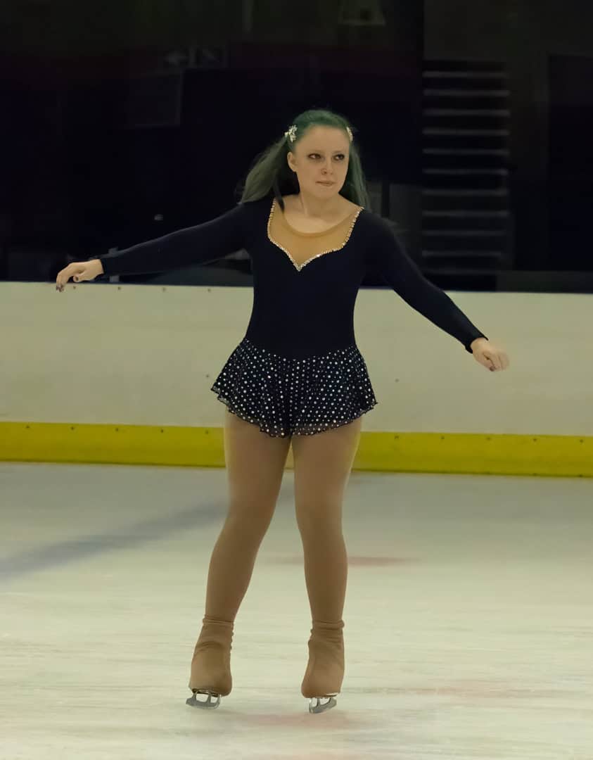 A female figure skater in a black costume with rhinestones, practicing on ice
