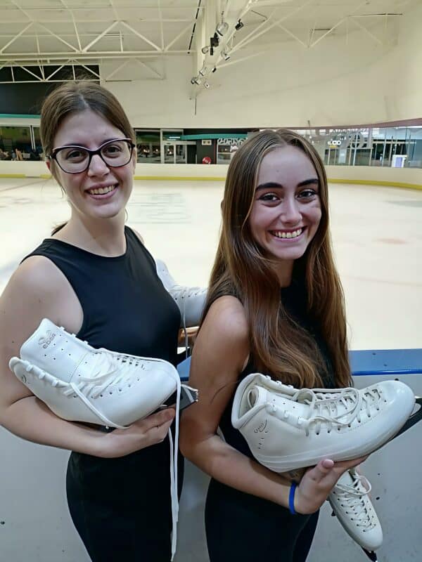 two woman smiling and holding ice skating shoes