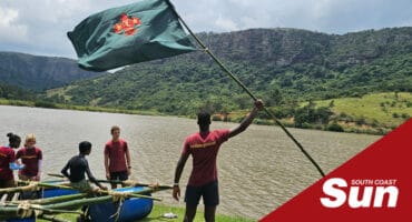 a boy holding a flag, people next to him in a makeshift raft near a river
