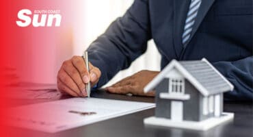 a stock image of a person with a contract and pen, and a model house.