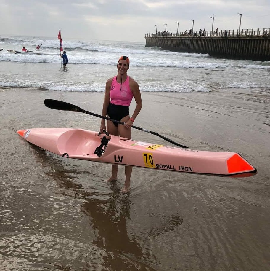 a woman holding her kayak and paddle on the beach